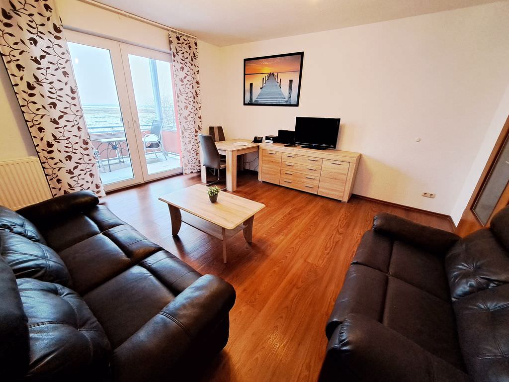 Ein Appartement für Familien mit zwei Ledersofas und einem Couchtisch dazwischen. Licht fällt durch das bodentiefe Fenster links in den Raum.