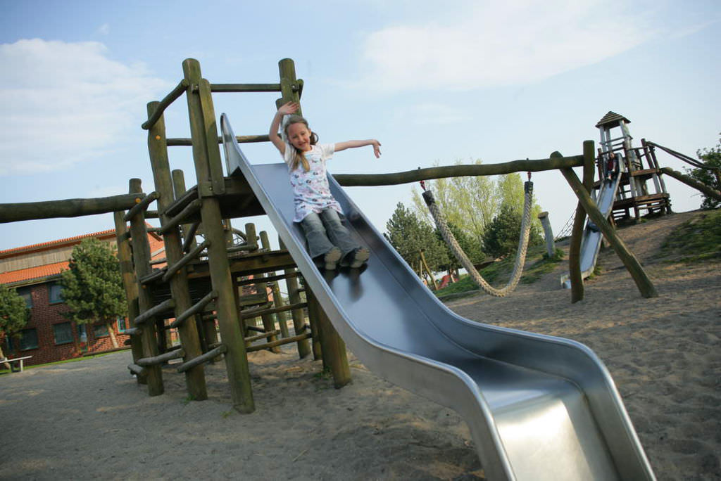Ein Mädchen rutscht winkend eine Rutsche herunter.