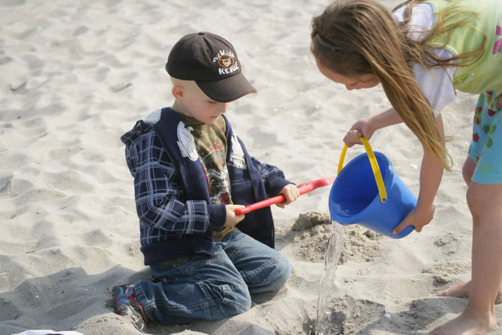 Ein Mädchen und eine Junge spielen im Sand des Ostseestrandes mit Eimer und Schaufel.