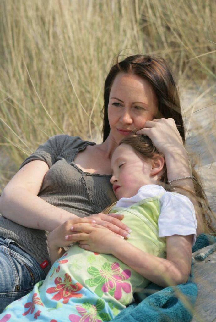 Mutter und Tochter liegen dicht nebeneinander in einer Düne zwischen hohen Gräsern.