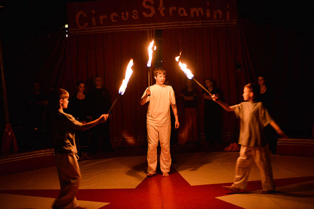 Drei Jungen stehen mit brennenden Fackeln im Kreis in einer Zirkusmanege.
