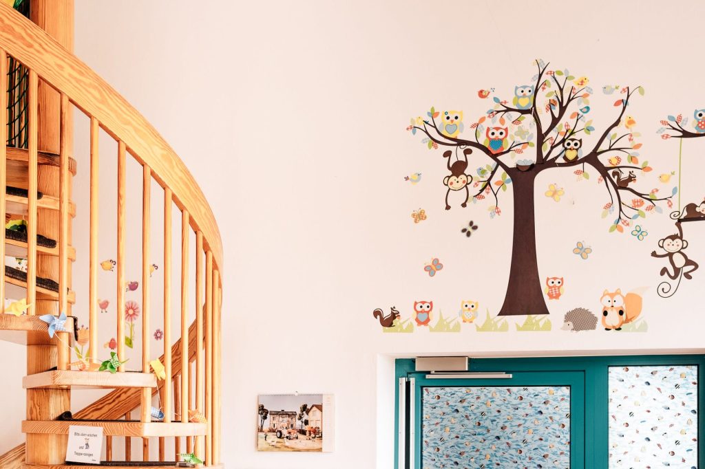 Links eine Holzwendeltreppe, vor Kopf eine Glastüre im Anschnitt, darüber an der Wand ein gemalter Baum mit unterschiedlichen Tieren.